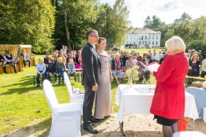 Brautpaar, Standesbeamtin und Gäste im Garten eines Schlosses bei der Trauung.
